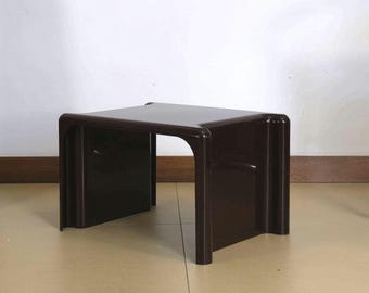 May include: A dark brown, square side table with rounded corners. The table has a simple, modern design and is made of a solid, glossy material. The table is approximately 46 cm wide, 46 cm deep, and 41 cm tall.