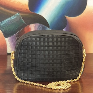 May include: A black quilted shoulder bag with a gold chain strap. The bag has a square pattern and is made of a soft, textured material.