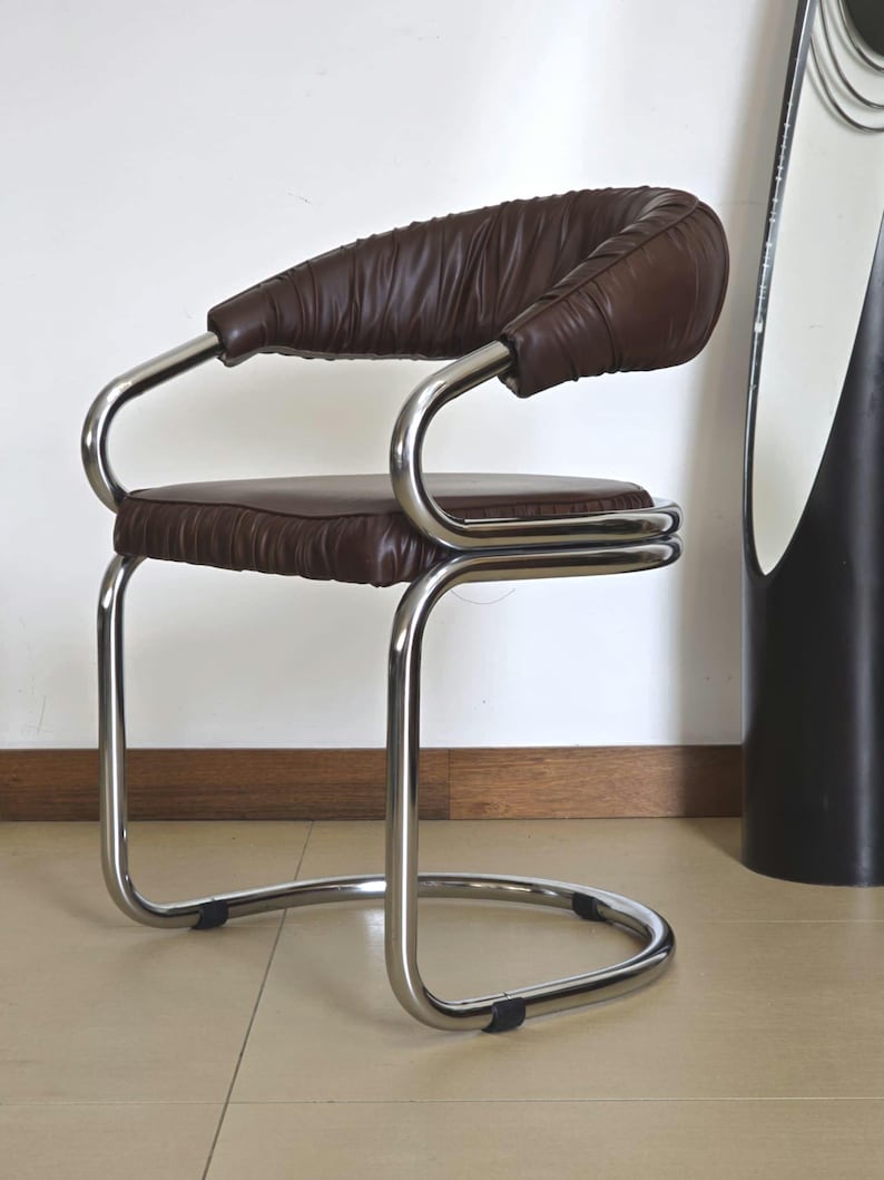 May include: A brown leather chair with a chrome frame. The chair has a curved back and a padded seat. The chair is on a tiled floor.