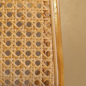 May include: Close-up of a woven cane chair seat with a natural wood frame. The cane is woven in a tight, intricate pattern, creating a durable and stylish surface.