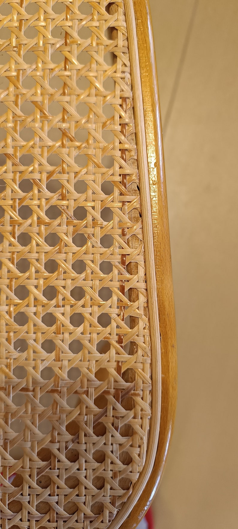 May include: Close-up of a woven cane chair seat with a natural wood frame. The cane is woven in a tight, intricate pattern, creating a durable and stylish surface.