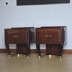 May include: A pair of dark wood bedside tables with brass detailing. Each table features a rectangular design with a drawer and a curved base. The brass base adds a touch of elegance. The tables are positioned next to each other.