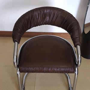 May include: A brown leather chair with a chrome frame. The chair has a curved back and a padded seat. The chair is designed in a modern style.