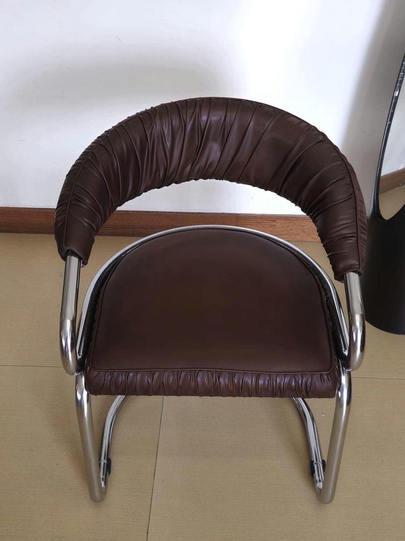 May include: A brown leather chair with a chrome frame. The chair has a curved back and a padded seat. The chair is designed in a modern style.