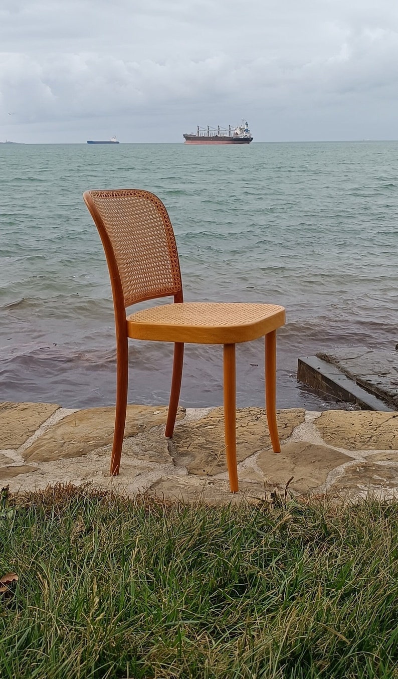May include: A wooden chair with a woven cane seat and back. The chair is sitting on a stone patio overlooking a body of water with a ship in the distance.