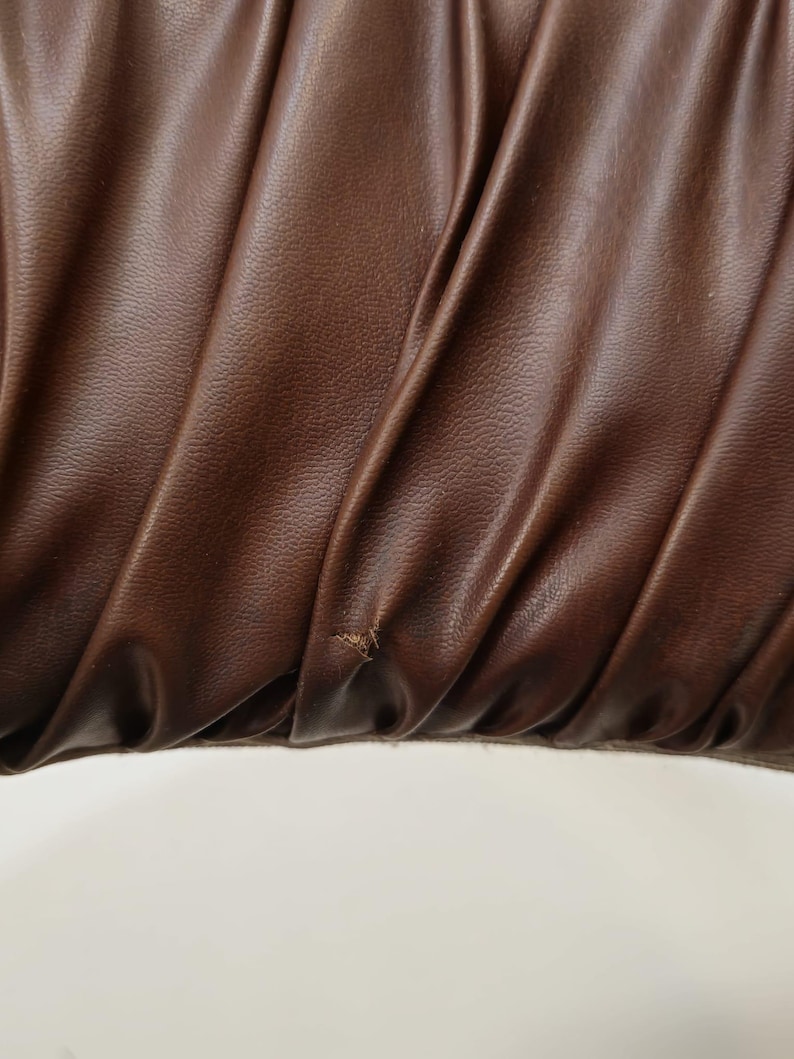 May include: Close-up of a brown leather fabric with a textured surface. The fabric is folded and has a slight wrinkle in the center.