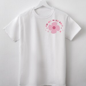 May include: White t-shirt with a pink flower graphic and the text "In My Wife Era" in a pink, rainbow-colored font.