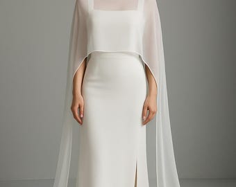 Puede incluir: Un vestido blanco largo hasta el suelo con escote cuadrado y una abertura lateral alta. El vestido se superpone con una capa blanca transparente y diáfana que cae sobre los hombros y se extiende hasta el suelo, creando largos paneles fluidos.