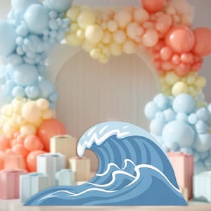 May include: A blue wave-shaped decoration with white accents, set against a backdrop of pastel-colored balloons arranged in an arch. The scene includes several small, wrapped gift boxes in the foreground, suggesting a celebratory theme.