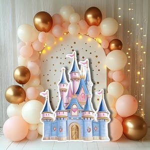 May include: A fairytale-themed party backdrop featuring a castle cutout in blue, pink, and gold, surrounded by balloons in similar colors. The backdrop includes a gold-colored arch and string lights, creating a whimsical atmosphere.