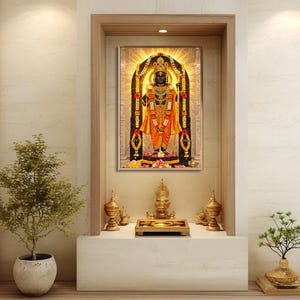 May include: A framed religious artwork showing a deity in orange and gold robes, with detailed jewellery. The artwork is set in a recessed alcove, with brass ornaments and small potted plants, creating a peaceful atmosphere.