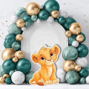 Può includere: Un ritaglio di cartone animato di un cucciolo di leone con un'espressione sorridente, ambientato su uno sfondo di palloncini verde acqua, oro e marmorizzati. I palloncini sono disposti a forma di arco, con un arco bianco sullo sfondo.