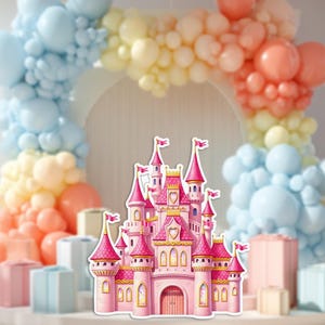 May include: A pink and gold castle cutout with multiple turrets and flags. The castle has heart-shaped details and arched windows. A colorful balloon arch in pastel colours is in the background, along with gift boxes.