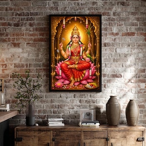 May include: A framed wall art print depicting a Hindu deity with four arms, wearing a red and gold sari and ornate jewelry, seated on a large pink lotus flower. The figure is positioned within a golden archway with a glowing halo background.