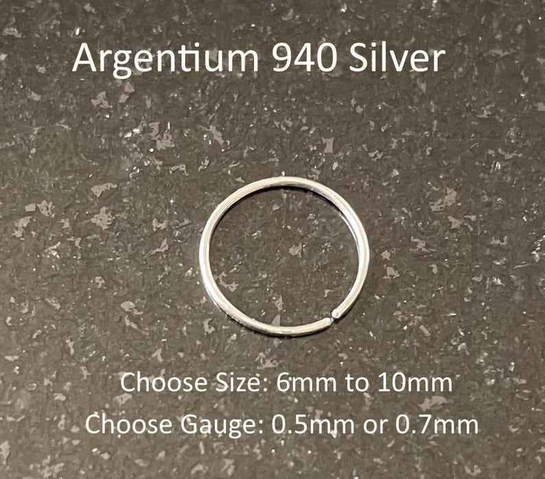 May include: A thin, circular Argentium 940 silver hoop ring. The text reads: Argentium 940 Silver, Choose Size: 6mm to 10mm, Choose Gauge: 0.5mm or 0.7mm. The silver ring is a simple, continuous band with a small gap, showcasing a metallic finish.