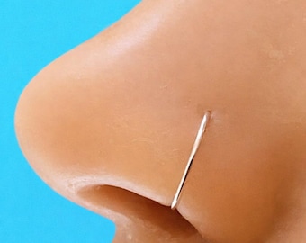 May include: A thin, circular metallic nose ring hoop with a polished silver-toned finish. The jewelry is positioned as a continuous, seamless band that rests against the skin, forming a simple, minimalist circular shape for facial piercing.