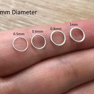 May include: Four silver-colored metal jump rings with a 6mm diameter, displayed in varying wire thicknesses labeled 0.5mm, 0.6mm, 0.8mm, and 1mm. These circular findings are arranged in a row, showcasing the different gauge options available for jewelry making.