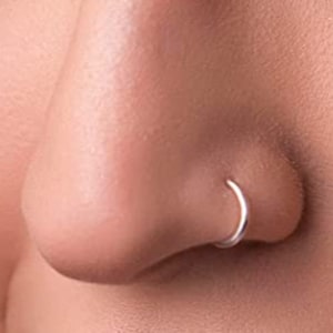 May include: A thin, circular silver nose ring hoop positioned in the nostril. The jewelry features a smooth, polished metallic finish and a simple, continuous band design that forms a complete circle when worn in the nasal piercing.