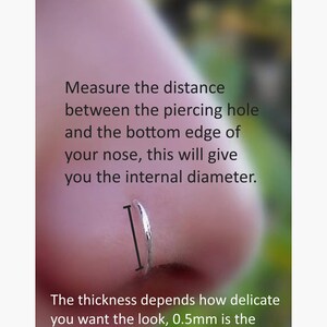 May include: A silver nose ring with a black measurement line indicating the internal diameter. Text reads: What size do I need? Measure the distance between the piercing hole and the bottom edge of your nose, this will give you the internal diameter. The thickness depends how delicate you want the look, 0.5mm is the thinnest, but is also more bendy.