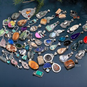 May include: A selection of gemstone pendants in diverse shapes and colours, including oval, teardrop, and rectangular designs. The pendants feature silver metalwork and a variety of stones, such as turquoise, amethyst, and quartz. The pendants are displayed on a dark blue surface.