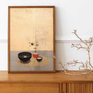 May include: A framed painting of a still life with a black bowl, a red vase, and a small blue bowl. The bowl contains a single pink flower and a sprig of green leaves. The painting is set against a light yellow background.