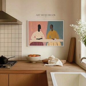 Pu&ograve; includere: Una stampa artistica astratta con due figure sedute a un tavolo. L'opera d'arte ha uno sfondo rosa e verde acqua con il testo "ART MUSE DECOR" sopra la stampa incorniciata. Le figure sono raffigurate in uno stile minimalista.