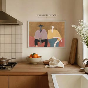 May include: A framed wall art print titled ART MUSE DECOR featuring a stylized illustration of two figures sitting side by side. One figure wears a hat, a light purple top, and black pants. The other figure wears a yellow top and blue pants.