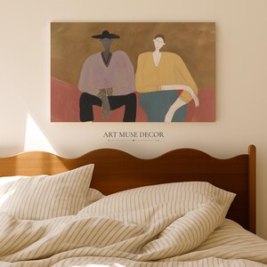 May include: A rectangular wall art print featuring two figures sitting side-by-side against a brown background. The left figure wears a wide-brimmed hat, a light purple V-neck top, and black trousers. The right figure wears a yellow long-sleeved top and a teal skirt.