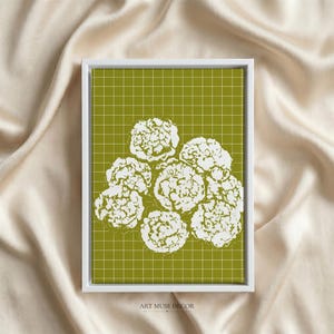 Op de afbeelding: Een rechthoekig ingelijst kunstwerk aan de muur met een witte bloemenillustratie van gegroepeerde bloesems, gecentreerd op een olijfgroene achtergrond met een dun wit rasterpatroon. De tekst ART MUSE DECOR staat onderaan in kleine zwarte letters.