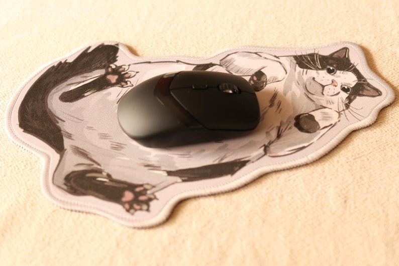 May include: A black computer mouse resting on a mousepad featuring a cartoon illustration of a white and black cat with a surprised expression.