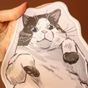 May include: A white and black cat with large eyes and a surprised expression is printed on a white fabric patch. The patch has a white stitched border.