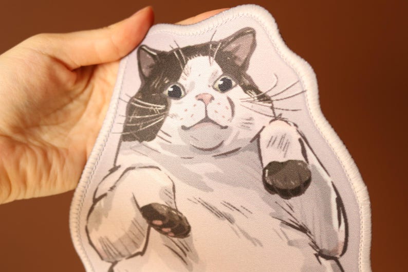 May include: A white and black cat with large eyes and a surprised expression is printed on a white fabric patch. The patch has a white stitched border.