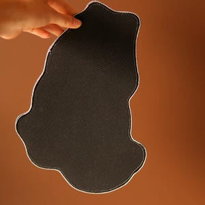 May include: Black fabric mouse pad with a unique, irregular shape. The pad is made of a soft, textured material.