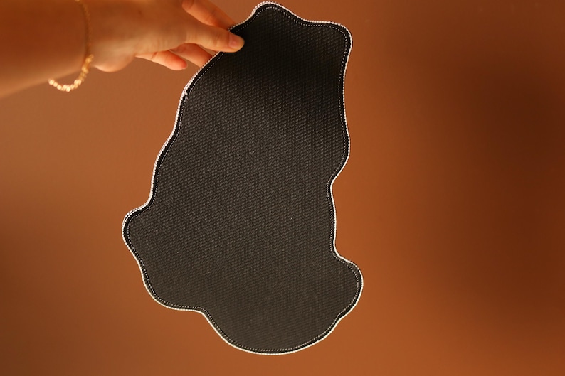 May include: Black fabric mouse pad with a unique, irregular shape. The pad is made of a soft, textured material.