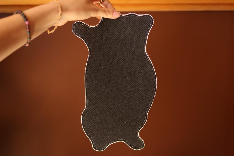 K&ouml;nnte beinhalten: Schwarze Stoff-Mausmatte in Katzenform. Die Mausmatte hat einen wei&szlig;en, gesteppten Rand.
