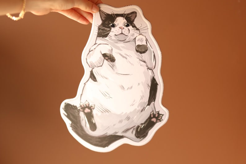 May include: A black and white cat illustration with a white background. The cat is lying on its back with its paws in the air. The cat has a round, fluffy body and a cute expression.
