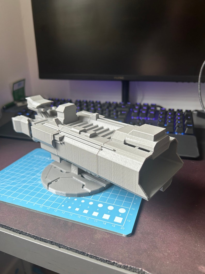 Puede incluir: Un modelo de nave espacial futurista impreso en 3D de color gris con un dise&ntilde;o detallado. La nave espacial est&aacute; sentada sobre una base circular y tiene un cuerpo largo y estrecho con una nariz puntiaguda.