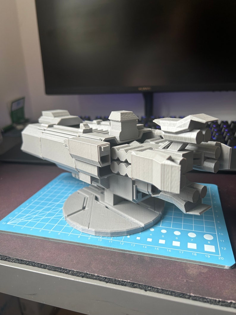 Puede incluir: Un modelo de nave espacial impreso en 3D de color gris con m&uacute;ltiples torretas y una base giratoria.