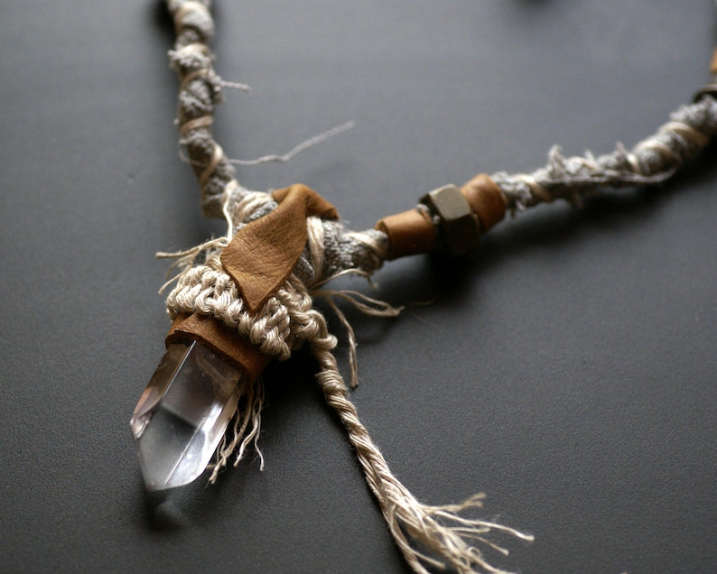 May include: A crystal point pendant necklace with a brown leather accent and a gray and brown rope chain.