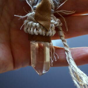 May include: A clear quartz crystal pendant wrapped in brown leather and beige macrame cord.