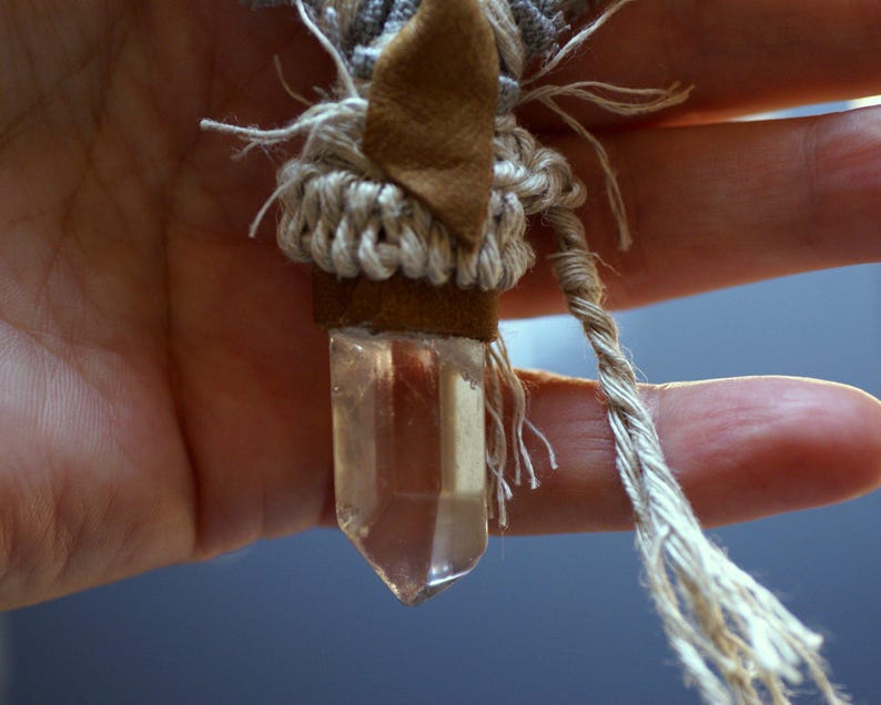 May include: A clear quartz crystal pendant wrapped in brown leather and beige macrame cord.