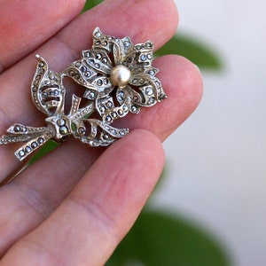 May include: A silver flower brooch with a pearl centre and marcasite stones.
