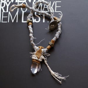 May include: A gray and white fabric necklace with brown beads and a clear quartz crystal pendant.