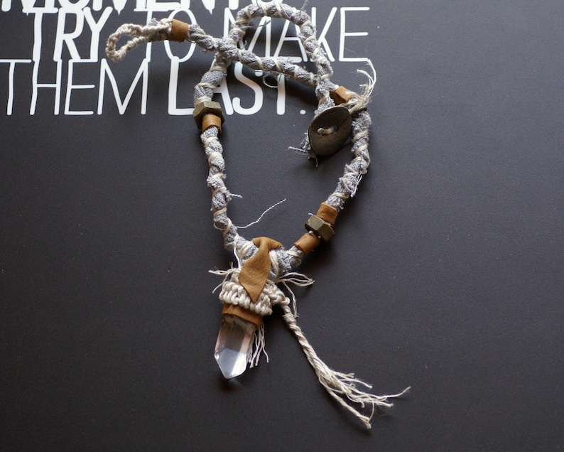 May include: A gray and white fabric necklace with brown beads and a clear quartz crystal pendant.