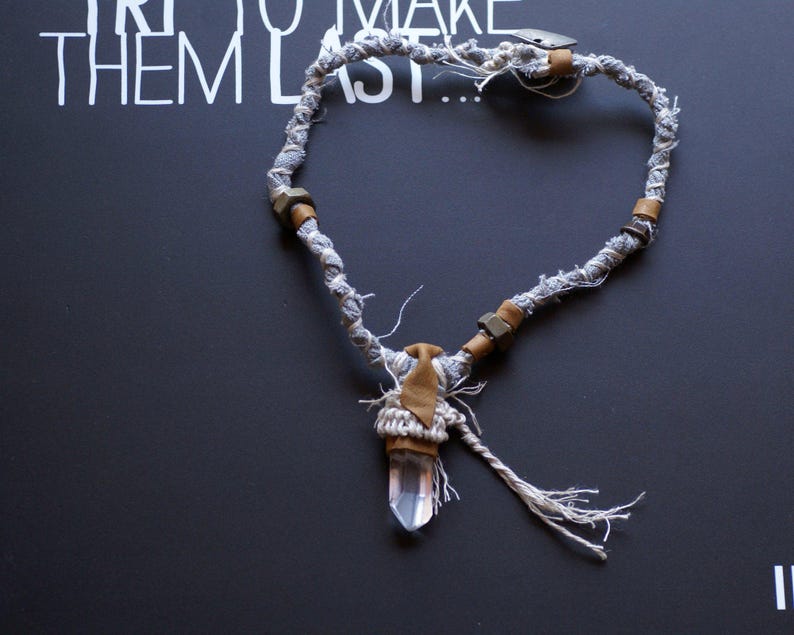 May include: A gray and brown fabric necklace with a crystal pendant. The necklace has a tassel and is tied with a knot.