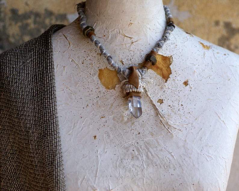 May include: A white crystal pendant necklace with a brown and white fabric wrap and brown beads. The necklace is on a white mannequin.