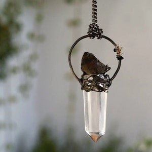 May include: A silver pendant necklace with a clear quartz crystal point, a small brown stone, and wire wrapped details.