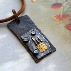 May include: A silver and gold pendant necklace with a textured, rustic look. The pendant features a small gold rectangle with a circuit board design and four silver rivets.