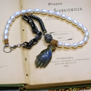 Puede incluir: Un collar de perlas blancas con una cadena de plata y un dije de mano de piedra azul. El collar está sobre un libro con el texto "PISMA SIENKIEWICZA TOM X QUO VADIS cz".