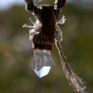 May include: A clear quartz crystal pendant hanging from a brown leather cord with a knotted rope detail.